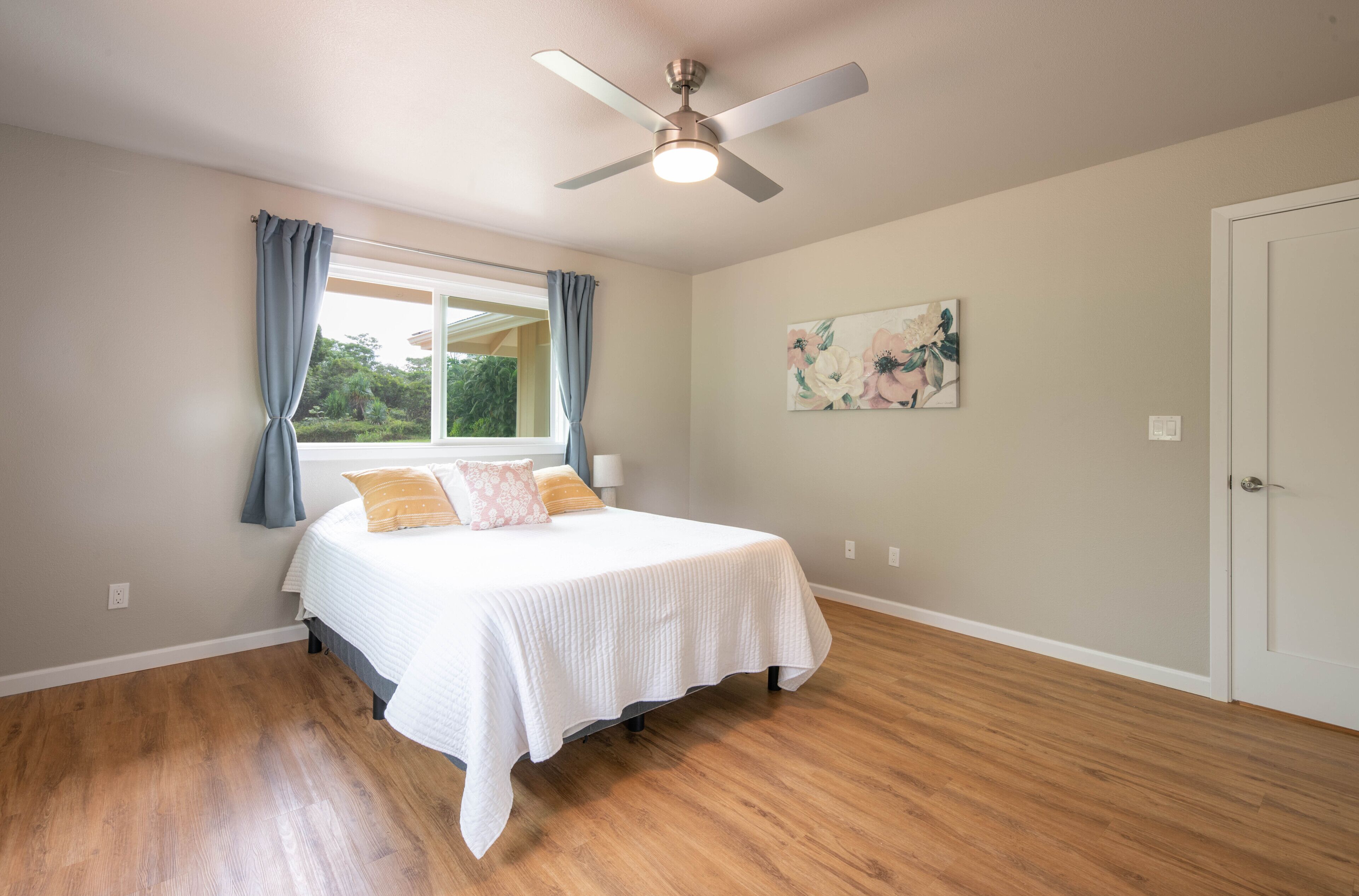 Un dormitorio con cama, ventilador de techo, ventana con cortinas y puerta.