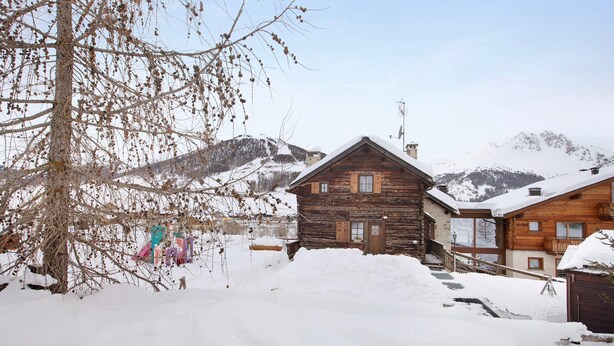 A wooden cabin with a snow-covered roof, a staircase leading to the entrance, and a mountain backdrop. - Apartment 'Gemma' with Mountain View, Shared Garden and Wi-Fi (Livigno)