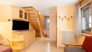 A room with a wooden staircase, a television, a sofa, and a radiator. - Apartment 'Gemma' with Mountain View, Shared Garden and Wi-Fi (Livigno)
