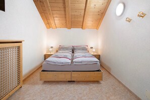 A bedroom with a wooden ceiling, a bed with white bedding, two bedside tables, and a wooden cabinet.