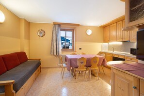 A compact living space with a sofa, dining table, chairs, a kitchen area, and a window with curtains.