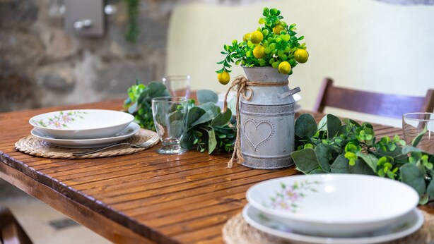 A wooden dining table with plates, glasses, and a decorative plant in a metal pot. - Apartment "Viviana's Holiday Home" with Wi-Fi (TRINITA D'AGULTU E VIGNOLA)
