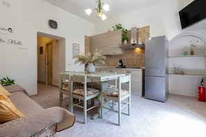 A modern kitchen with a dining table, chairs, a refrigerator, and a TV mounted on the wall.
