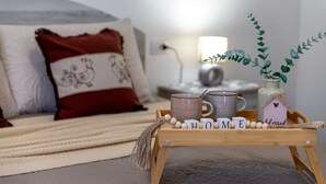 A cozy bedroom with a bed, pillows, a bedside table with a lamp, and a tray with mugs and a decorative house. - Apartment "Viviana's Holiday Home" with Wi-Fi (TRINITA D'AGULTU E VIGNOLA)