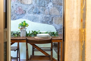 A dining table set with a white plate, a glass, and a vase with green foliage.