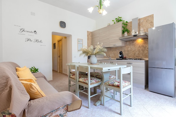 A modern kitchen with a built-in stove, a stainless steel refrigerator, and a dining area with a white table and floral chairs.
