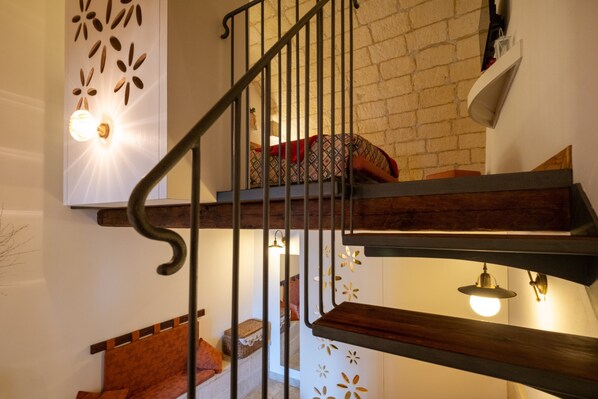 A staircase with a wooden handrail and metal balusters, a patterned cushion on the landing, and wall-mounted lighting fixtures.