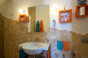 Une salle de bain avec un mur en pierre, un lavabo blanc, un miroir et un sèche-cheveux.