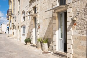 Un bâtiment en pierre avec une porte, des fenêtres et une petite plante près de l’entrée.