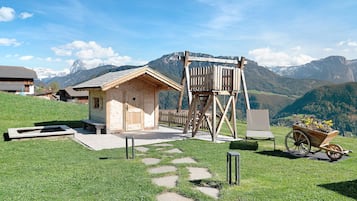 Eine Holzhütte mit einer Holzleiter, einem Blumen-Schubkarren und einem steinernen Weg, der dorthin führt.