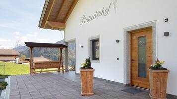 Ein Gebäude mit einer Holzpergola, einer Holztür und zwei Holzpflanzgefäßen mit Blumen.