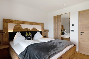 A wooden-framed bed with white bedding, a bedside table with a lamp, and a wooden door.