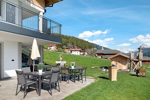 Un patio con mobiliario exterior, una estructura de madera y vistas a casas y montañas.