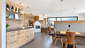 A modern kitchen with wooden cabinets, a built-in wine rack, and a dining area with wooden chairs and a bench. - Holiday Apartment 'Platiederhof Apt Lajen' with Mountain View, Shared Garden & Wi-Fi (Laion)