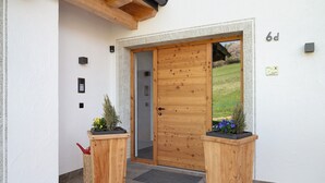 A wooden door with a glass panel, a small outdoor area with a wooden bench and potted plants, and a stone-tiled entrance. - Holiday Apartment 'Platiederhof Apt Lajen' with Mountain View, Shared Garden & Wi-Fi (Laion)