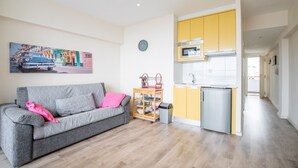 A living room with a sofa, a small kitchen area with yellow cabinets, a microwave, and a sink.