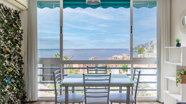 A balcony with a table and chairs, a view of the sea, and a plant wall.
