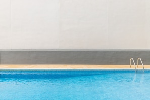 Une piscine avec un bord carrelé, une terrasse en bois et des échelles métalliques pour accéder à la piscine.