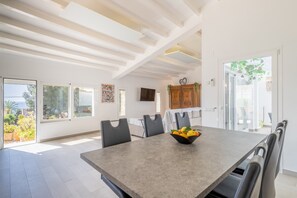 A spacious dining area with a long table, modern chairs, and a bowl of fruit.
