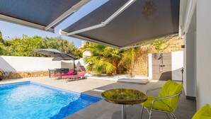 A swimming pool with lounge chairs and a table, a covered patio area, and a stone wall with greenery. - Villa "Bennu - Lujo Y Confort" near Beach with Private Pool & Wi-Fi (Calpe)