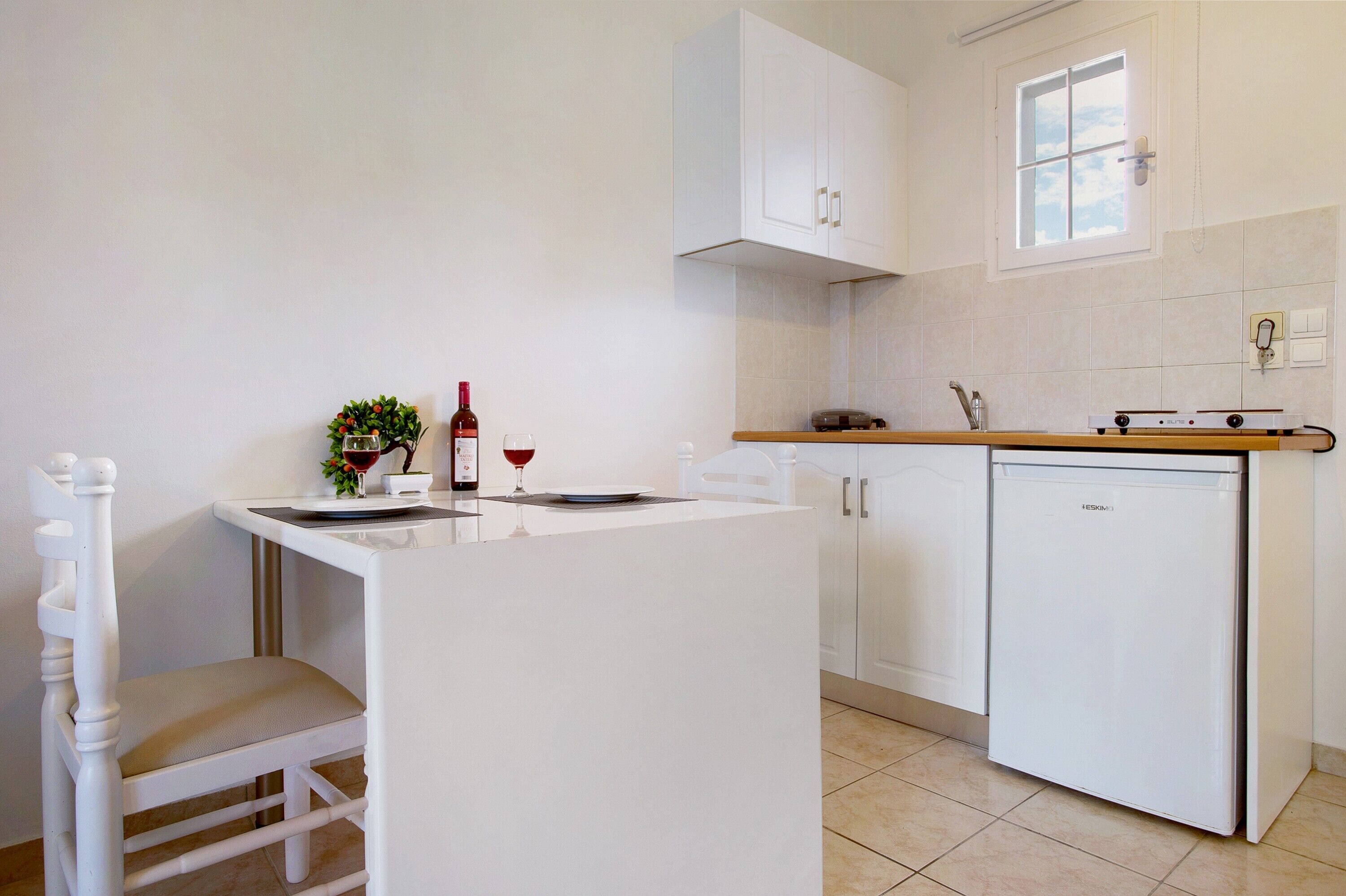 A compact kitchen with white cabinetry, a small island with a chair, a wine bottle, and a glass on the counter.