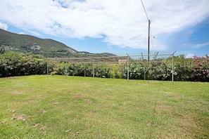 A grassy field with a greenhouse structure and a mountain in the background. - Holiday Apartment "Tropical 4" with Shared Garden, A/C & Wi-Fi (Zakynthos)