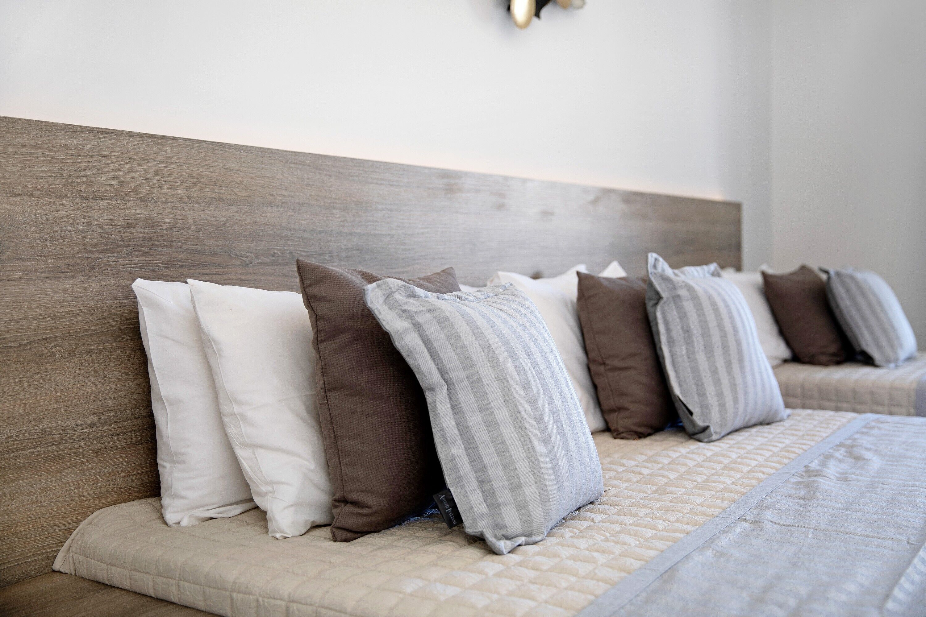 Ein Bett mit Kopfteil, mehreren Kissen und einer gesteppten Tagesdecke.
