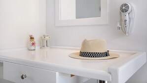 Un mobile bagno bianco con un cappello sopra, uno specchio, un asciugacapelli montato a parete e un piccolo vasetto decorativo.