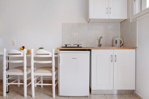 Une petite cuisine avec des meubles blancs, un réfrigérateur blanc, un plan de travail en bois et un évier.