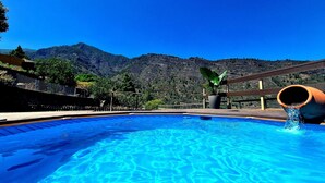Piscina com água azul cristalina, deck de madeira e montanhas ao fundo.