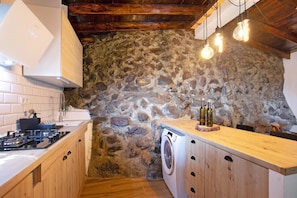 A kitchen with a stone wall, wooden cabinets, a washing machine, and hanging light bulbs. - Chalet "Laurelin" with Sea View, Private Mini Pool & Wi-Fi (Candelaria)