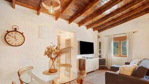 Uma sala de estar acolhedora com teto de madeira, uma mesa redonda de vidro, cadeiras de madeira, um sofá, uma televisão e uma lareira.