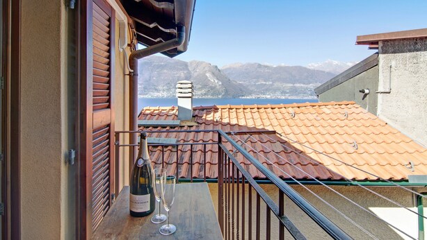A balcony with a bottle of wine and glasses, a tiled roof, and a mountainous view. - Holiday Home "Bernhouse" with Lake View, Balcony and Wi-Fi (Dorio)