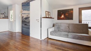 A room with a wooden floor, a white door, a grey sofa, and two framed pictures on the wall. - Holiday Home "Bernhouse" with Lake View, Balcony and Wi-Fi (Dorio)
