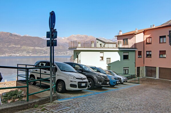 A parking area with cars, a building with balconies, and a mountainous backdrop.