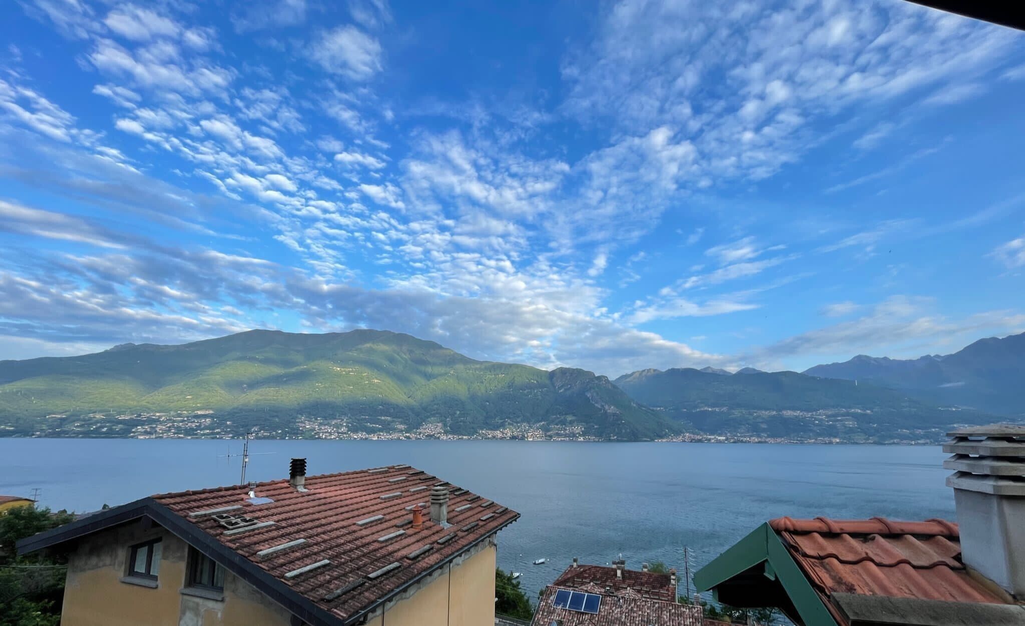 Ein See mit Bergen im Hintergrund, ein klarer Himmel und Gebäude mit roten Ziegeldächern.