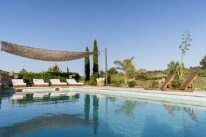 A pool with lounge chairs, a shaded area, and surrounding greenery.
