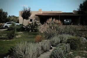 A house with a stone wall, a car parked outside, and a garden with various plants.