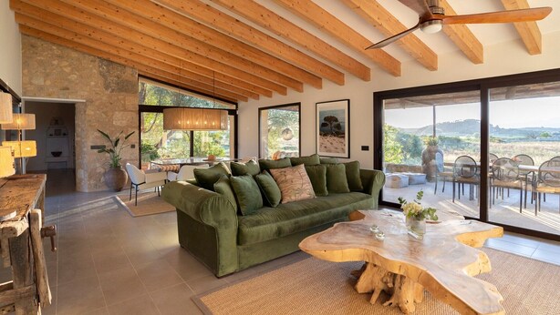 A spacious living area with a green sofa, wooden coffee table, and large windows offering a view of the outdoors.