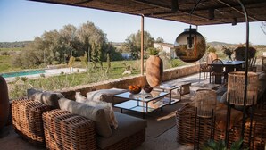 An outdoor patio with wicker furniture, a glass-top table, and a view of a pool and landscape.