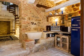 Une cuisine rustique avec un mur en pierre, un évier, un réfrigérateur bleu et un meuble en bois.