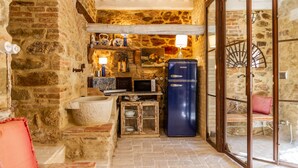 Une cuisine rustique avec un mur en pierre, des étagères en bois, un réfrigérateur bleu et une petite table à manger.