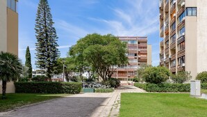 A residential area with a paved road, a tall evergreen tree, and a multi-story building with balconies.