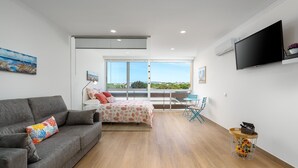 A modern bedroom with a bed, a sofa, a TV, and a balcony with a view.