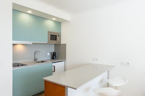 A modern kitchen with teal cabinets, a white countertop, a built-in microwave, a coffee machine, and a sink.