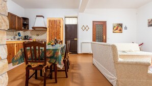 Zona de menjador amb una taula ben a punt per a quatre, caires de fusta, un sofà i una cuina al fons.