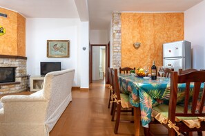 A dining area with a table set for four, a fireplace, a television, and a refrigerator. - Holiday Home "Casa Splendida" with Mountain View, Terraces & Wi-Fi (Monreale)