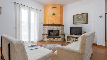 Un salon avec une cheminée, deux fauteuils, un téléviseur et un tableau accroché au mur.