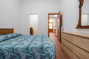 Un dormitorio con una cama, un aparador de madera, un espejo y una puerta que da a otra habitación.