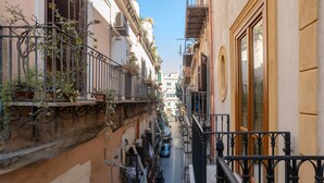 Un estrecho callejón entre edificios con balcones, una scooter estacionada en la calle y un cielo azul despejado.